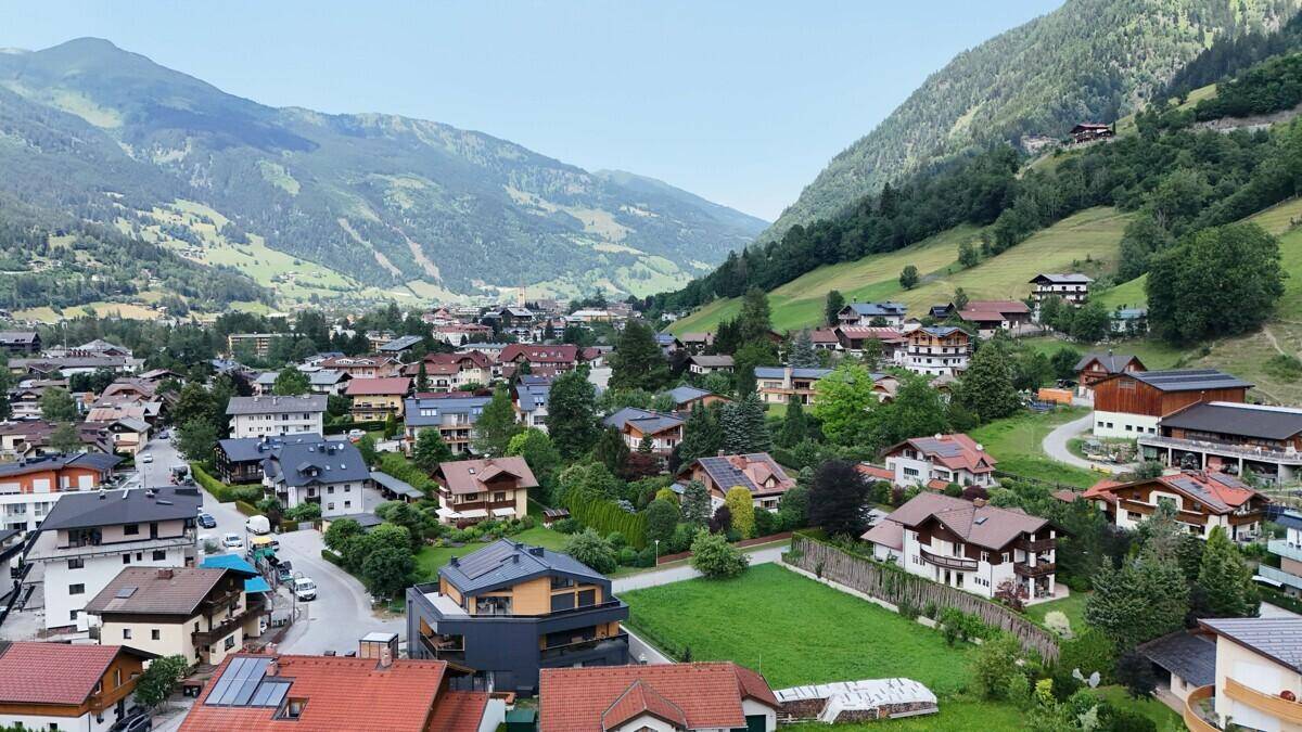 Panoramablick auf ein malerisches Dorf in einem Tal, umgeben von majestätischen Bergen und grünen Hängen.
