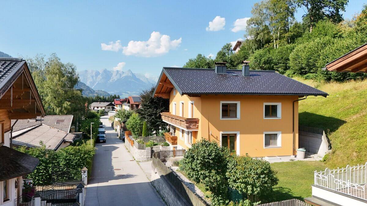 Das gelbe Haus mit dunklem Dach und Holzbalkonen, eingebettet in eine grüne Umgebung mit Bergblick.