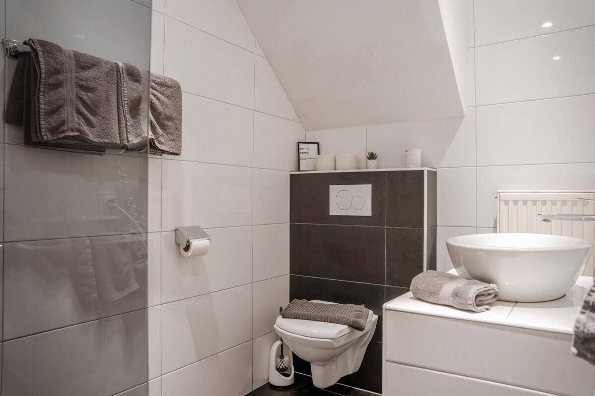 Modernes WC mit Wand-WC, Aufsatzwaschbecken und stilvollen Fliesen in Weiß und Grau.