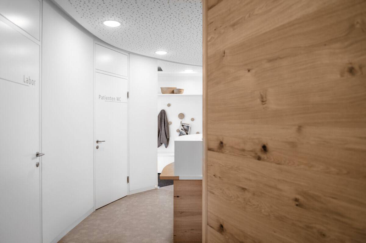 Heller Flur mit Holzwandelementen und Türen zu Labor und Patiententoilette, modern und funktional gestaltet.