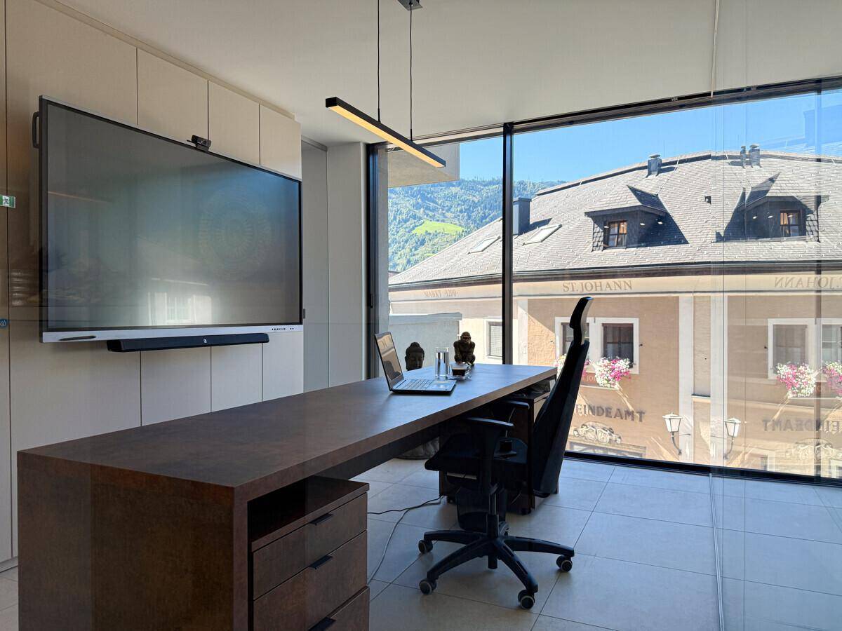 Helles Büro mit raumhohen Fenstern, modernem Schreibtisch und Bergblick.