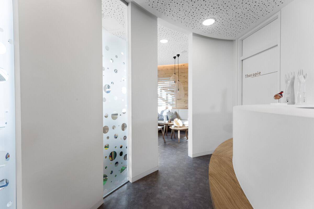 Heller Flur mit moderner Rezeption und Blick in einen Therapieraum, ausgestattet mit Milchglas-Schiebetüren.