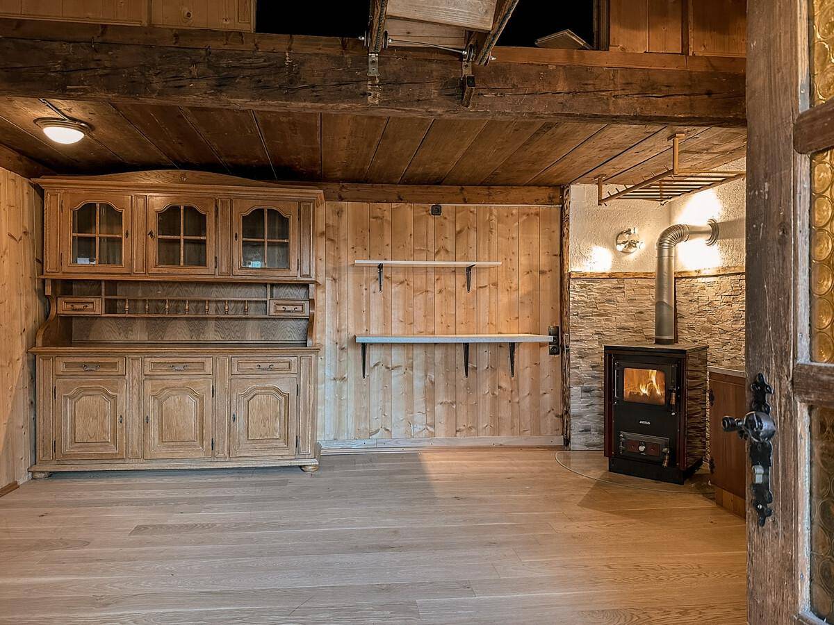 Gemütlicher Raum mit Holzboden, traditionellem Holzschrank und einem funktionierenden Holzofen als Heizquelle.