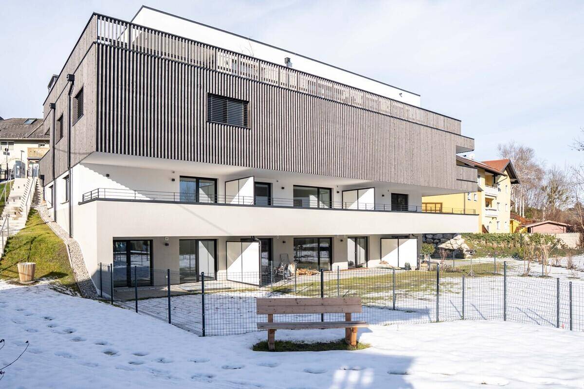 Moderne Wohnanlage mit Holzfassade und Balkonen, umgeben von einer verschneiten Landschaft.