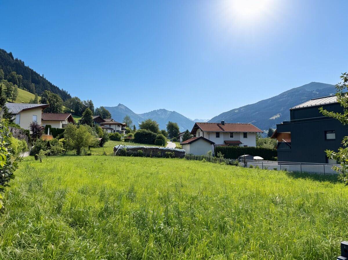 Weitläufige grüne Wiese mit Blick auf die umliegenden Berge und Häuser unter einem strahlend blauen Himmel.