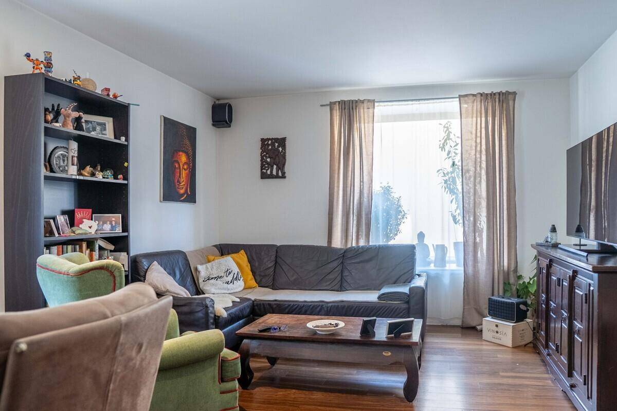 Gemütliches Wohnzimmer mit dunklem Ledersofa, Bücherregal und Holzboden.