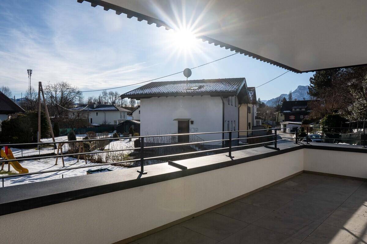 Sonniger Balkon mit Fliesenboden und Blick auf den verschneiten Gemeinschaftsgarten mit Spielplatz.