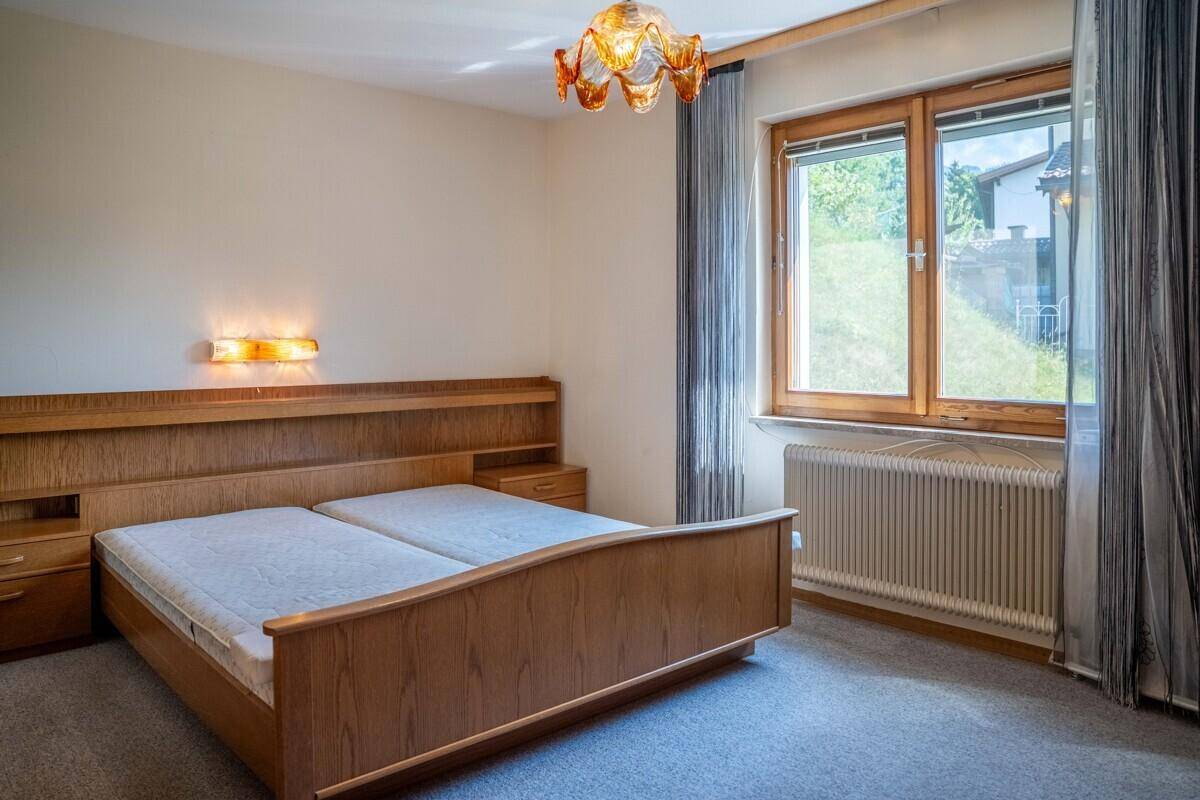 Schlafzimmer mit Doppelbett, Teppichboden und großem Fenster mit Blick ins Grüne.