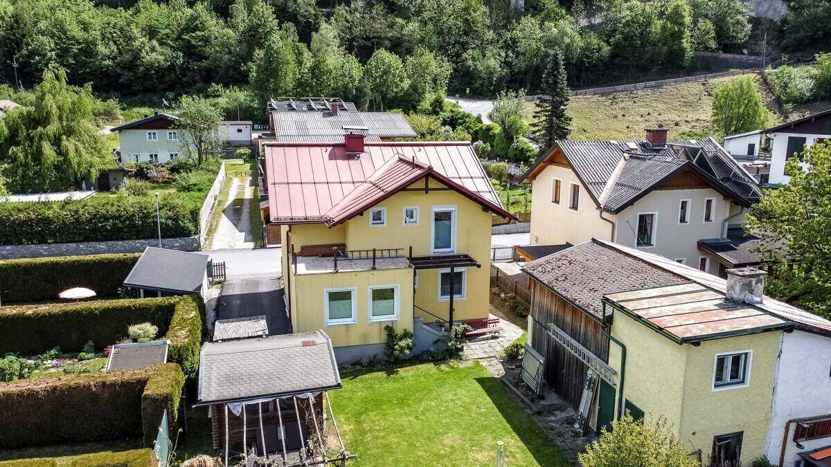 Erhöhte Ansicht des gelben Hauses mit rotem Dach, umgeben von weiteren Gebäuden und grünen Hügeln.