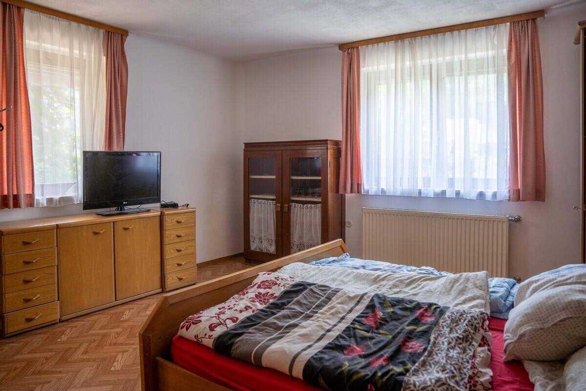 Gemütliches Schlafzimmer mit Holzmöbeln, Parkettboden und zwei großen Fenstern für viel Licht.