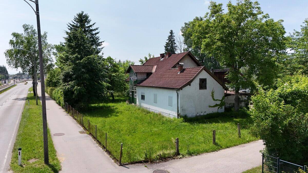 Einfamilienhaus mit hellblauer Fassade, rotem Ziegeldach und großem, ungenutztem Gartenbereich an der Straße.
