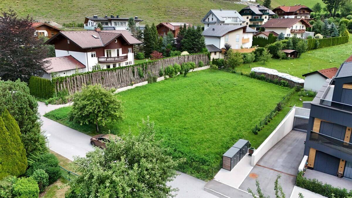 Großes grünes Grundstück in einer Wohngegend, umgeben von Häusern und bewaldeten Hügeln im Hintergrund.