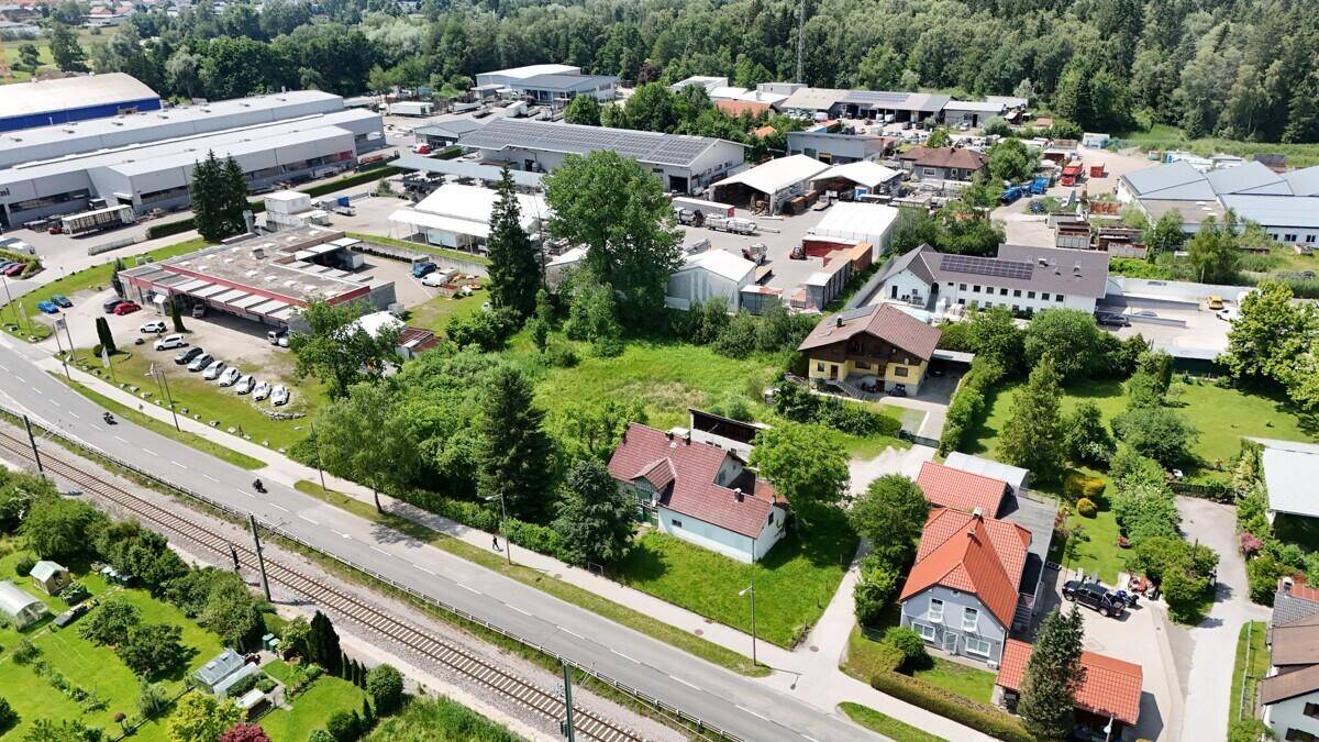 Übersicht aus der Luft mit Wohngebäuden, einer Straße und dahinterliegenden Gewerbebetrieben und Wald.