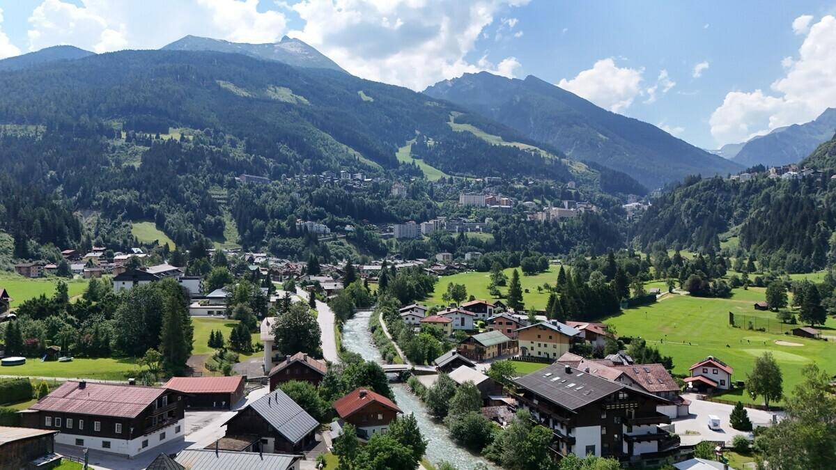 Weitläufiger Blick auf eine Bergstadt mit Fluss und grünen Tälern unter blauem Himmel.