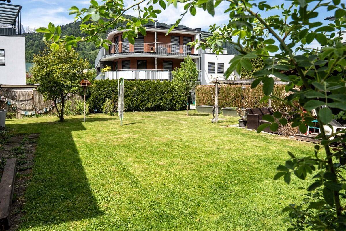 Weitläufiger Garten mit Rasenfläche und Blick auf moderne Gebäude mit Balkonen und Berge.