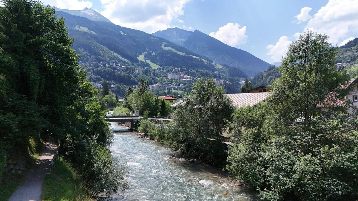 Flusslandschaft mit üppiger Vegetation und majestätischen Bergen im Hintergrund an einem sonnigen Tag.