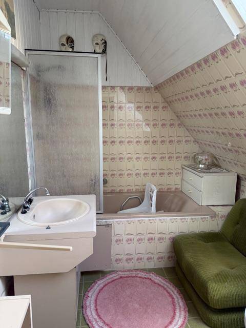 Badezimmer mit Badewanne, Waschbecken und Dusche unter der Dachschräge, gefliest in Pastellfarben.