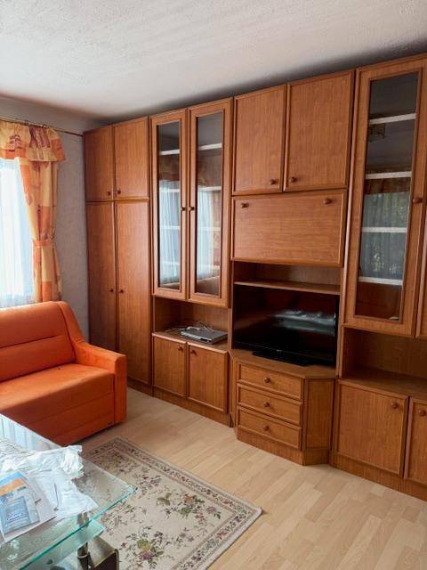 Wohnzimmer mit großer Holzschrankwand, integriertem Fernseher und orangefarbenem Sofa.