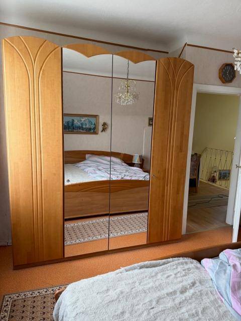 Schlafzimmer mit großem Holzschrank mit Spiegeltüren und Blick auf das Bett.