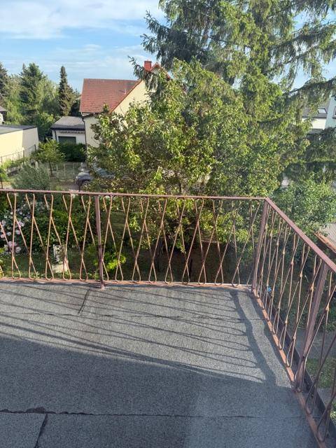 Kleiner Balkon mit Metallgeländer und Blick auf den Garten und die Nachbarschaft.