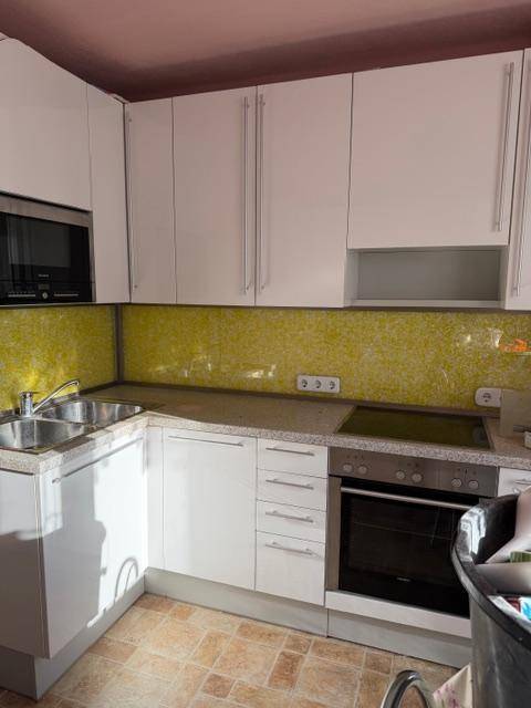 Moderne Küche mit Spüle, Kochfeld, Backofen und weißen Schränken.