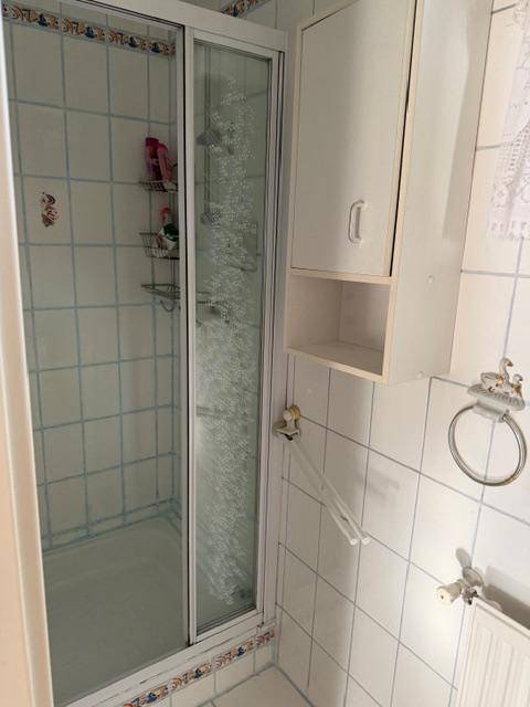 Badezimmer mit Duschkabine und weißen Fliesen mit blauen Akzenten.