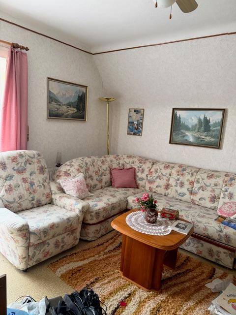 Wohnzimmer mit floral gemustertem Ecksofa, Couchtisch und Bildern an der Wand.