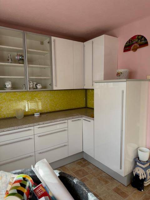 Moderne Küche mit weißen Hochglanzschränken, gelber Rückwand und rosa Wänden.