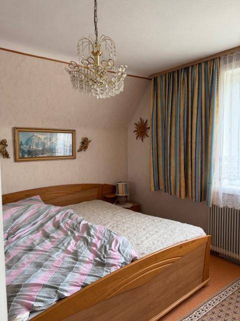 Gemütliches Schlafzimmer mit Holzbett, Kronleuchter und schrägen Wänden im Dachgeschoss.