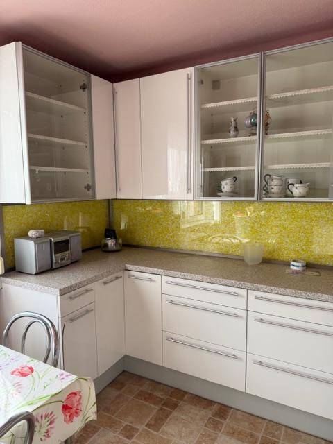 Moderne Küche mit weißen Schränken, gelber Spritzschutzwand und gefliestem Boden.