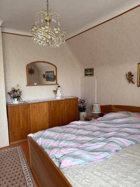 Schlafzimmer mit Holzbett, Kommode, Spiegel und Kronleuchter unter der Dachschräge.