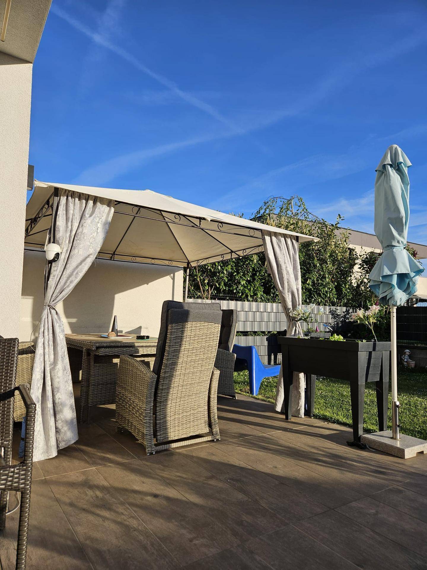 Sonniger Terrassenbereich mit Gartenmöbeln, Pavillon und Sonnenschirm.