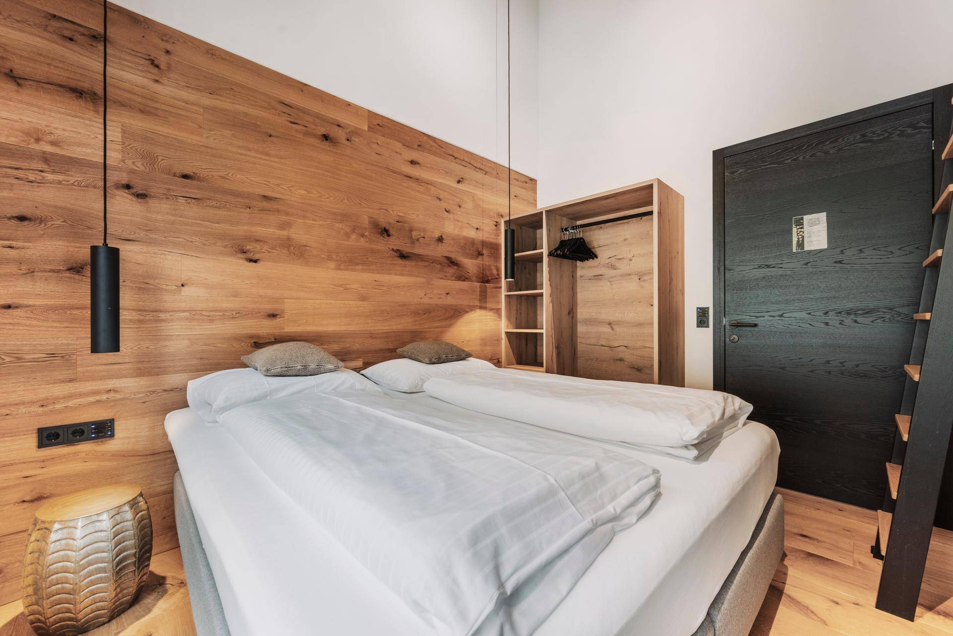 Schlafzimmer mit Holzwand, Doppelbett und offenem Kleiderschrank in modernem Design.