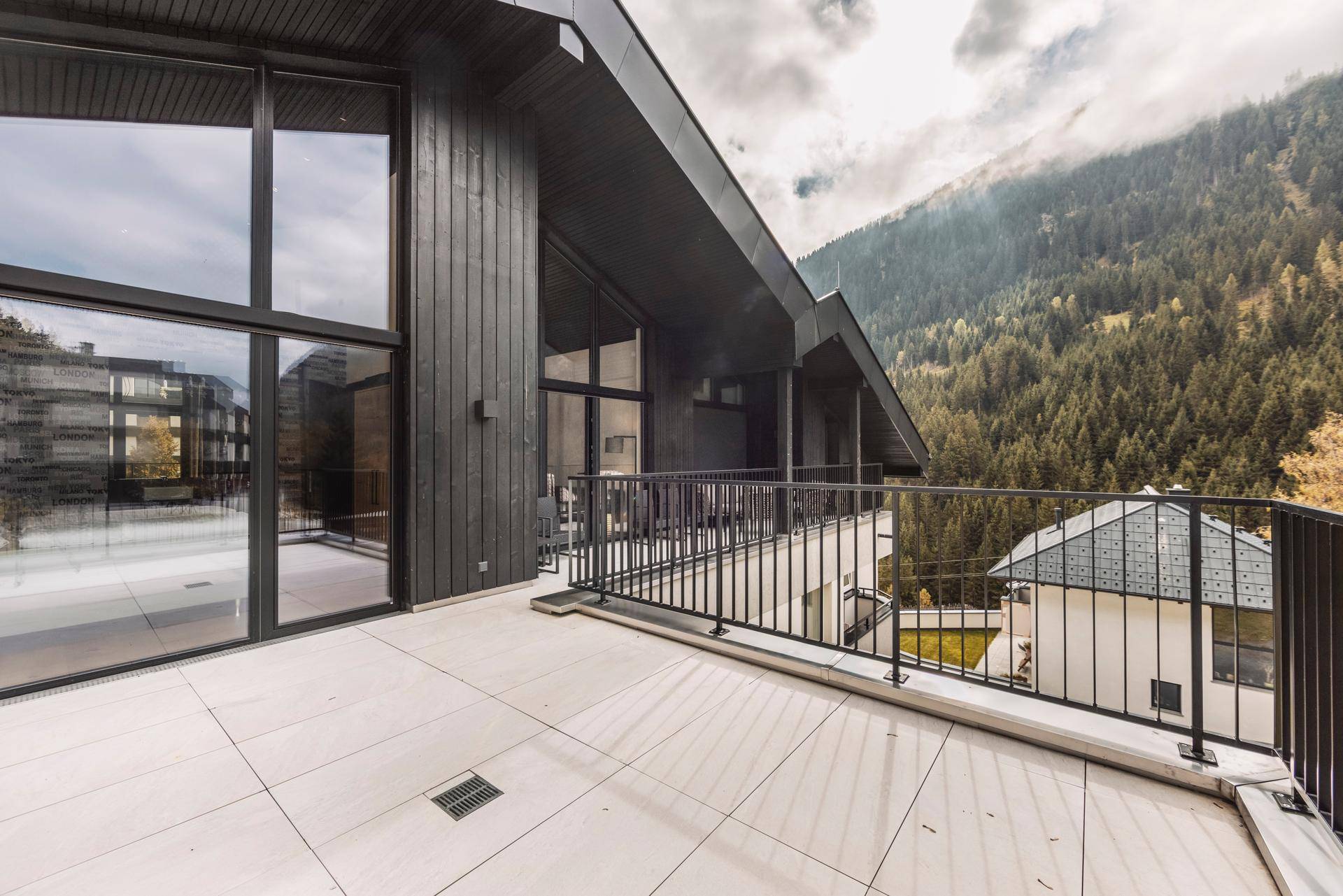 Große Terrasse mit Fliesenboden und modernem Geländer, umgeben von Berglandschaft.