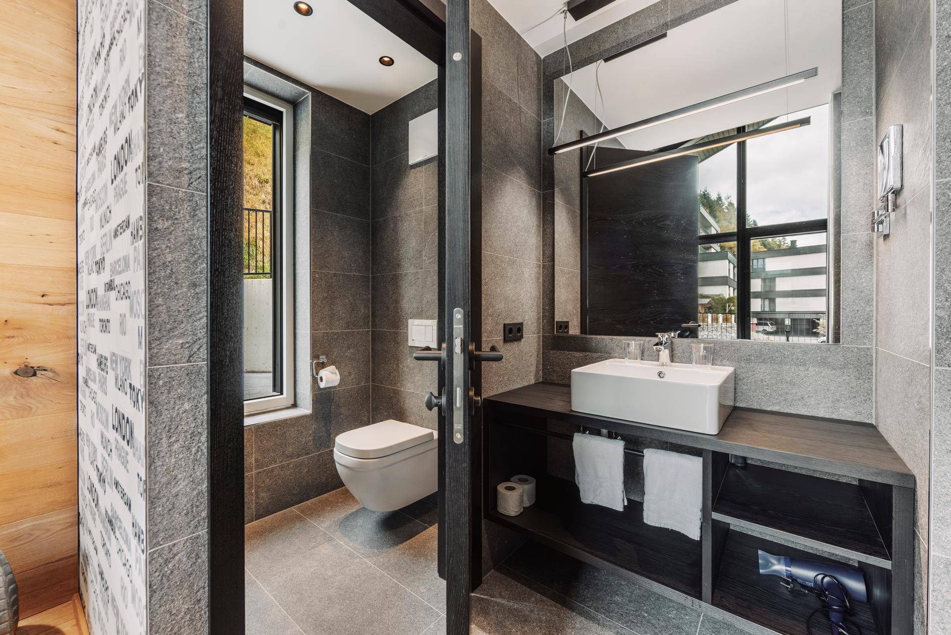 Modernes Badezimmer mit grauen Fliesen, wandhängendem WC und stilvollem Waschtisch.