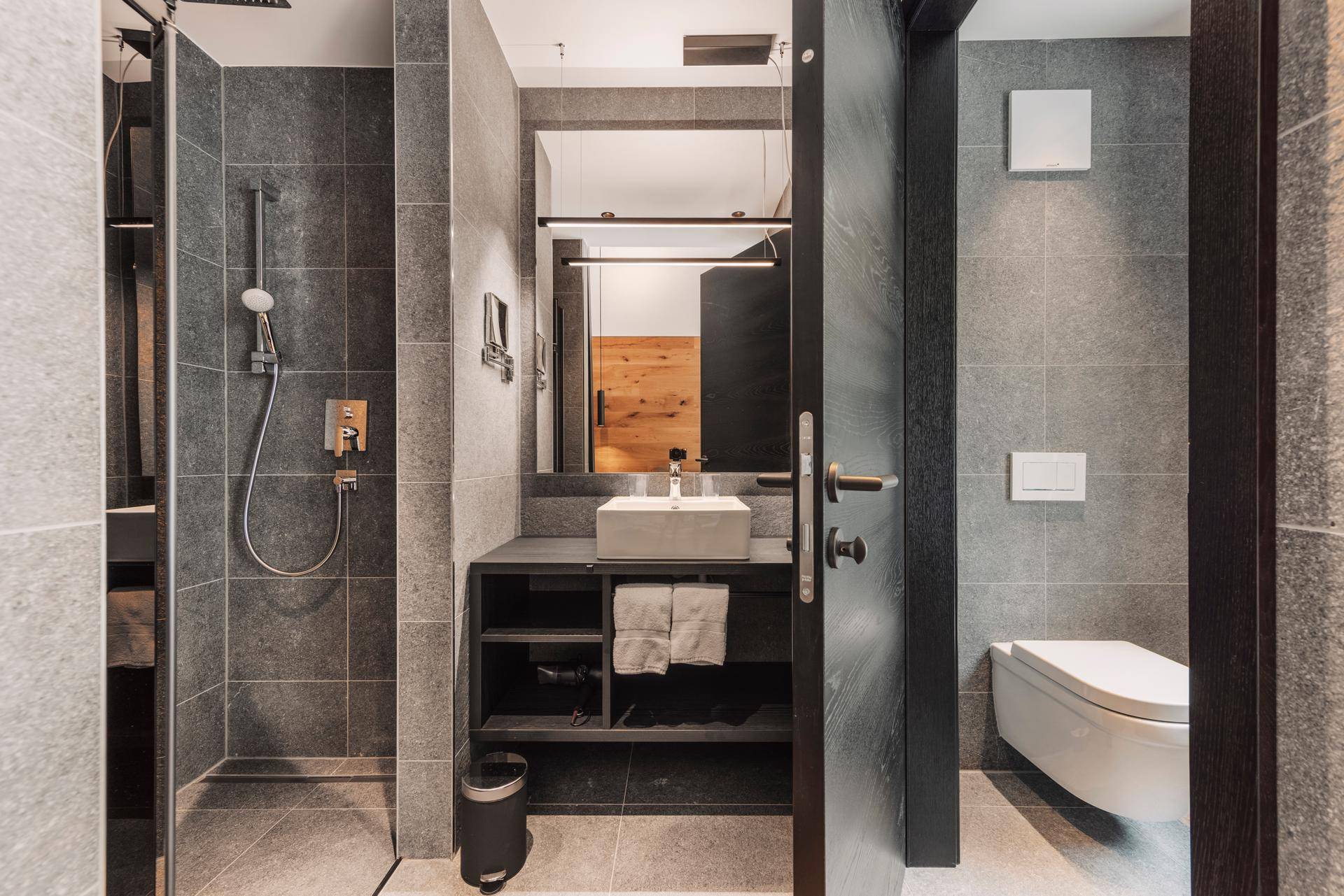 Modernes Badezimmer mit begehbarer Dusche, grauen Fliesen und elegantem Waschtisch.