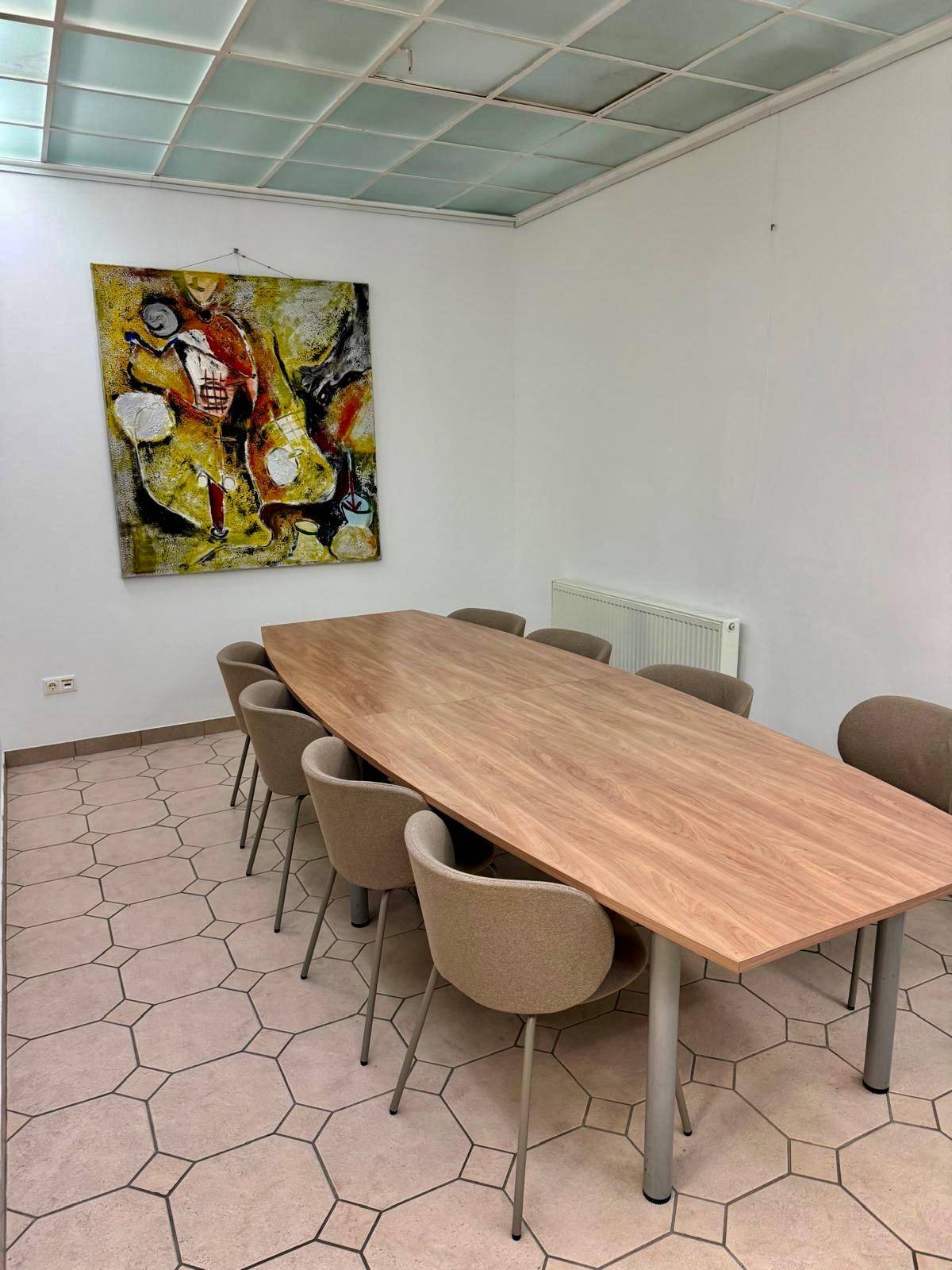 Konferenzraum mit großem Holztisch, bequemen Stühlen und einem modernen Kunstwerk an der Wand.
