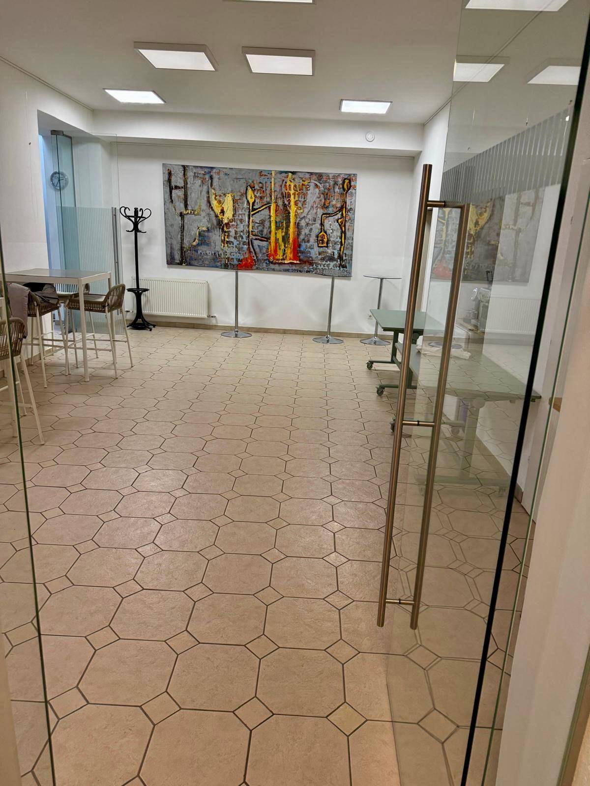 Geräumiger Empfangsbereich mit Fliesenboden, Stehtischen und moderner Kunst an der Wand.