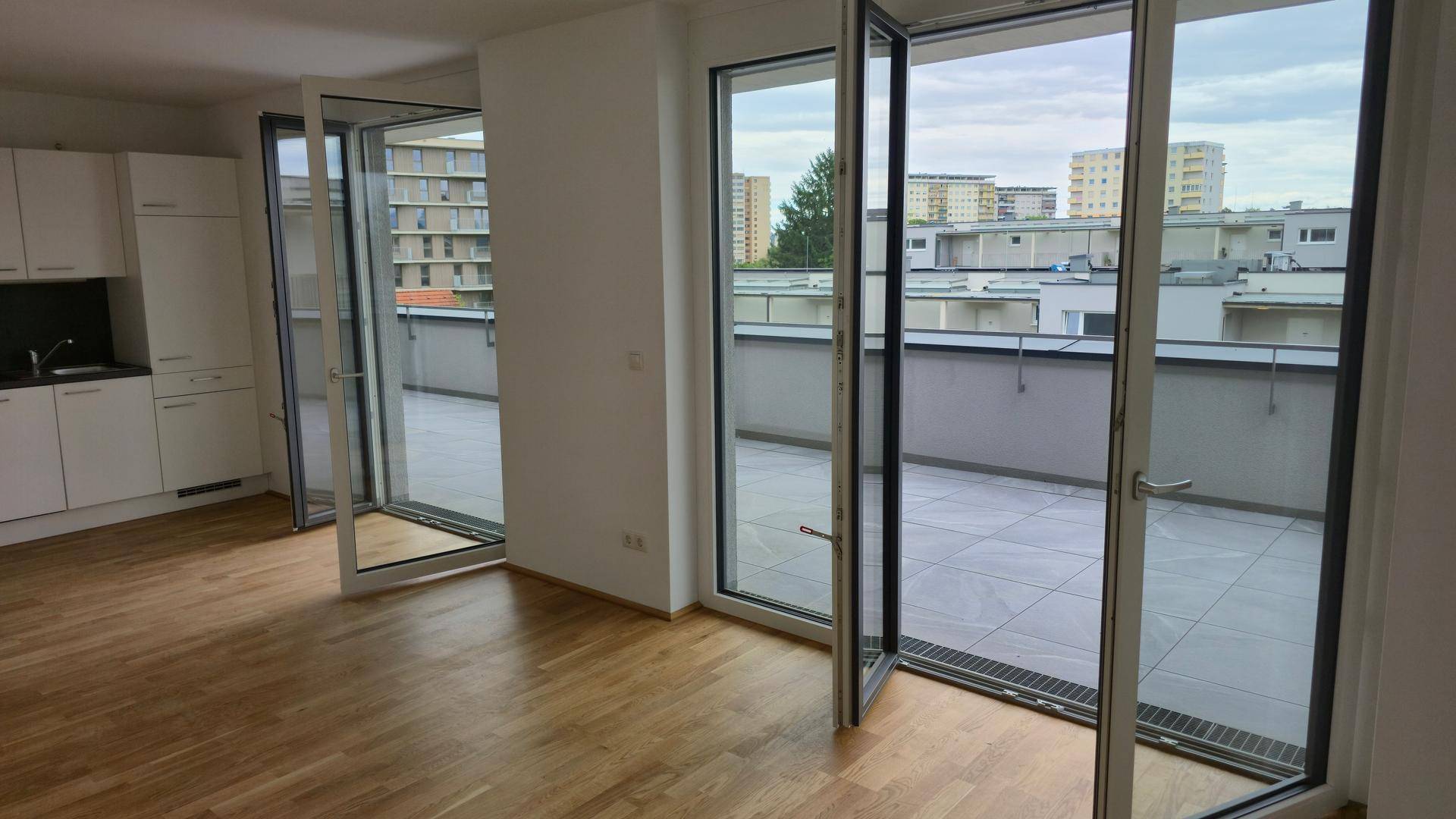 Heller Wohnbereich mit Holzboden, integrierter Küchenzeile und Zugang zur großen Terrasse.
