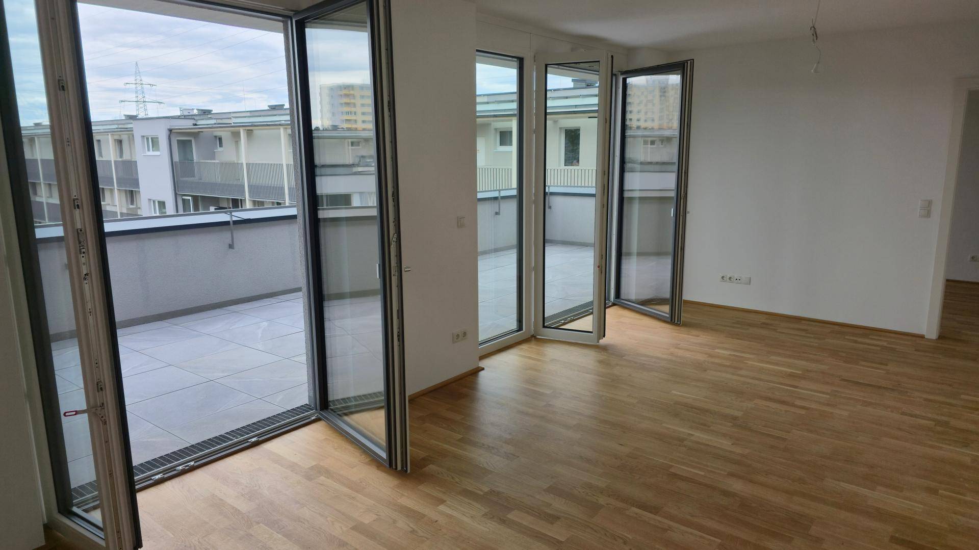Lichtdurchfluteter Wohnraum mit Parkettboden und raumhohen Fenstern, die zur Terrasse führen.