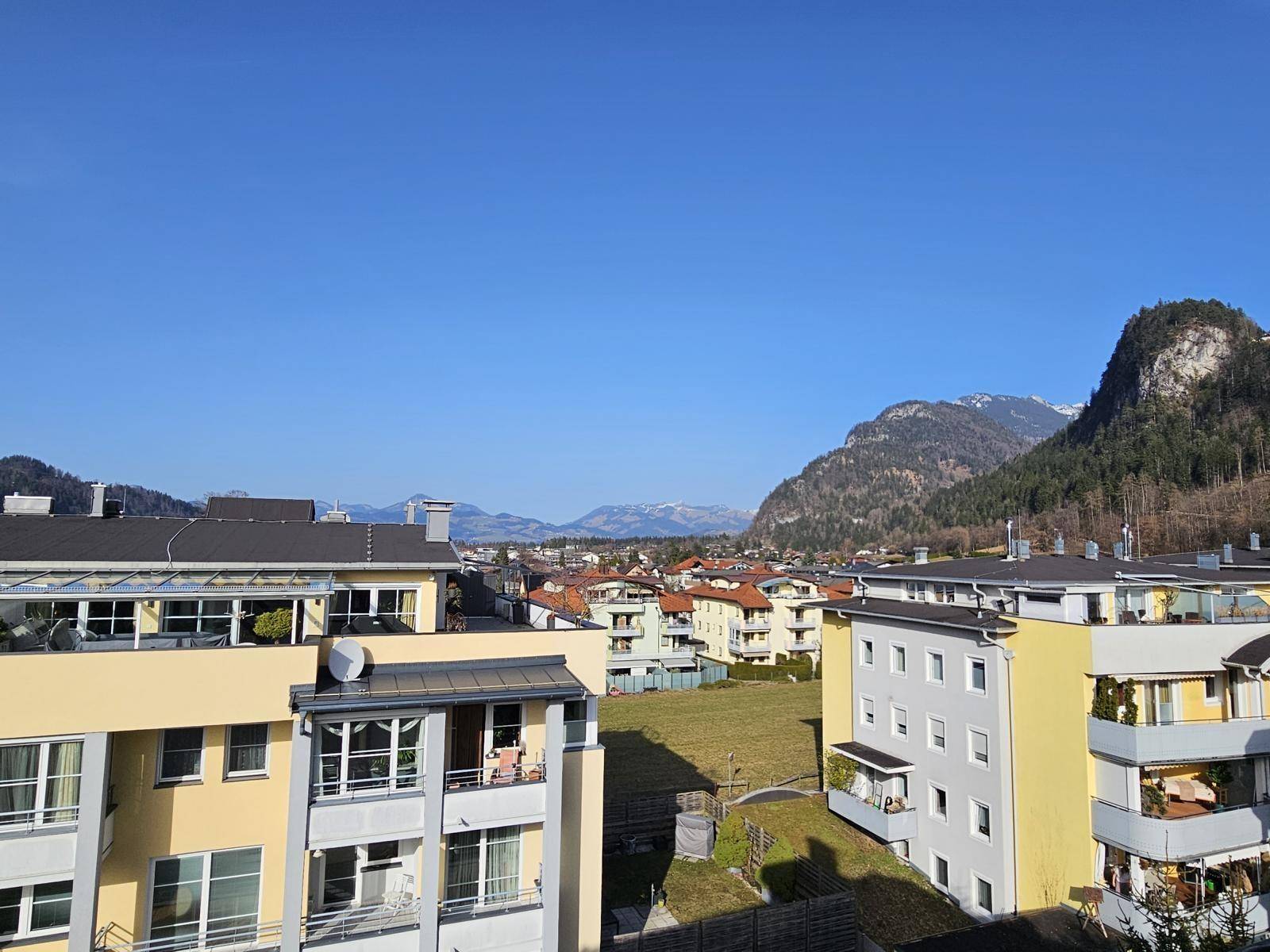 Weitläufiger Blick über die Dächer der Stadt auf die umliegende Berglandschaft unter blauem Himmel.