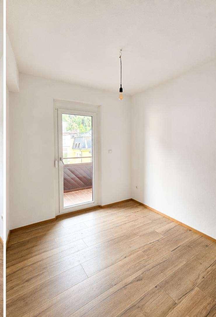 Helles Zimmer mit Balkonzugang und Holzfußboden, ideal als Schlaf- oder Arbeitszimmer.