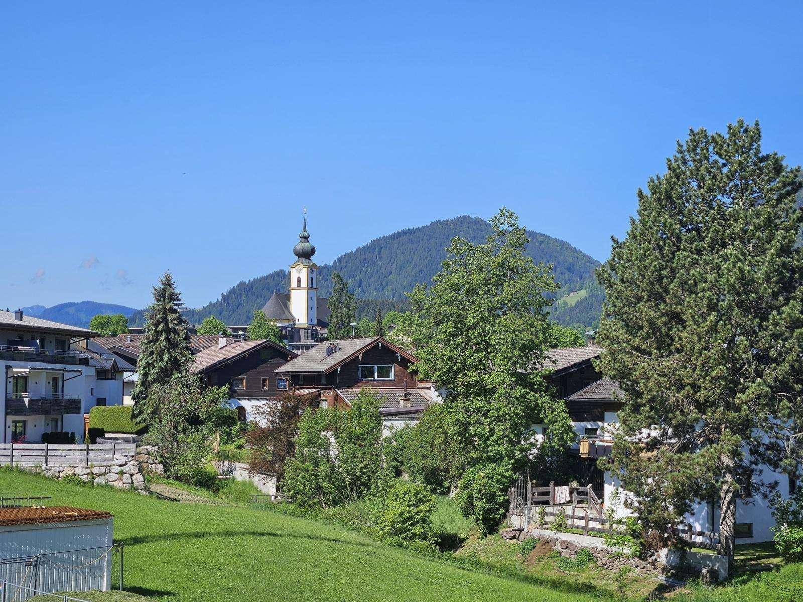 Panoramablick auf ein charmantes Dorf mit Kirche und umliegenden grünen Bergen.
