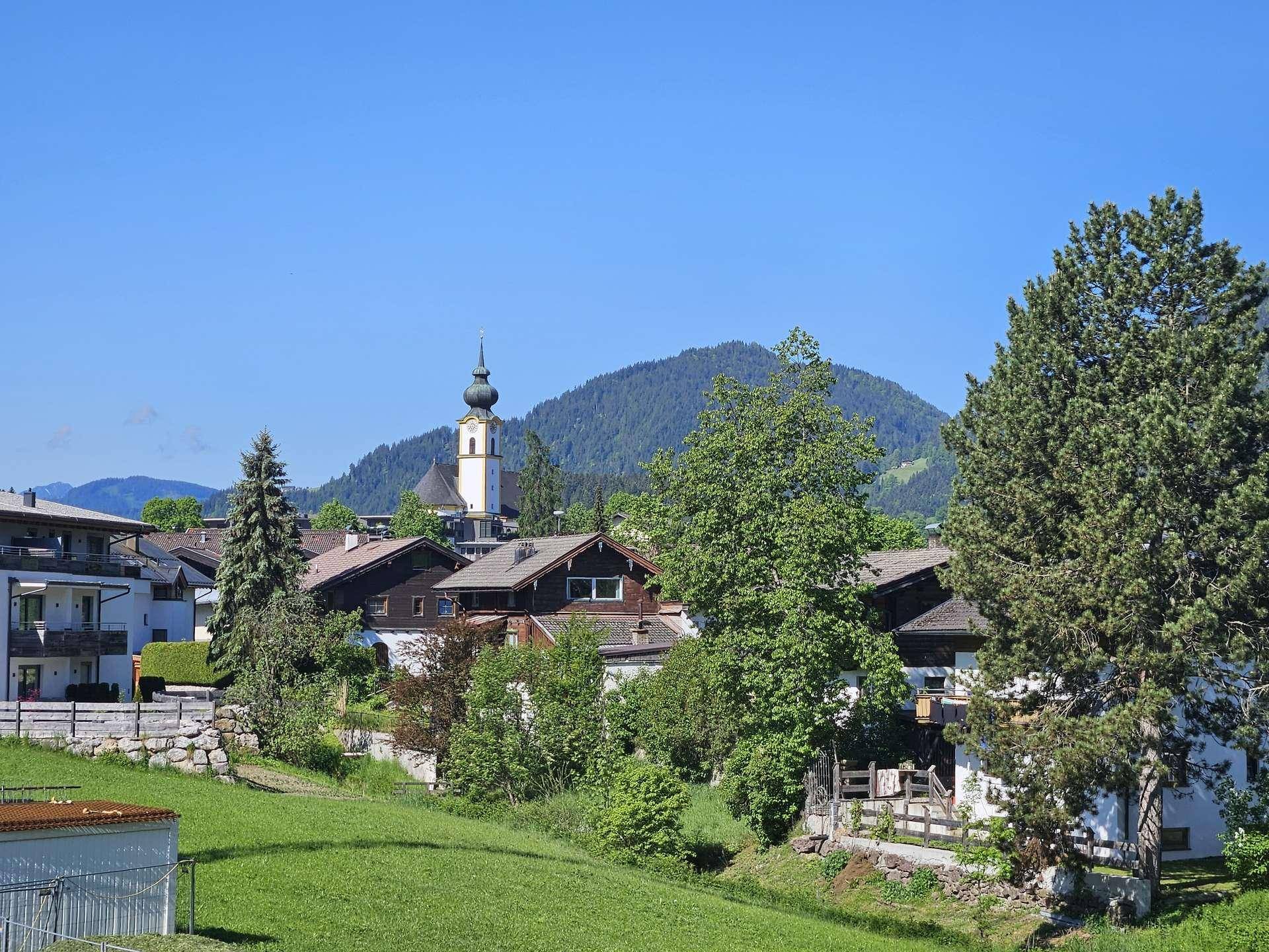 Panoramablick auf ein charmantes Dorf mit Kirche und umliegenden grünen Bergen.