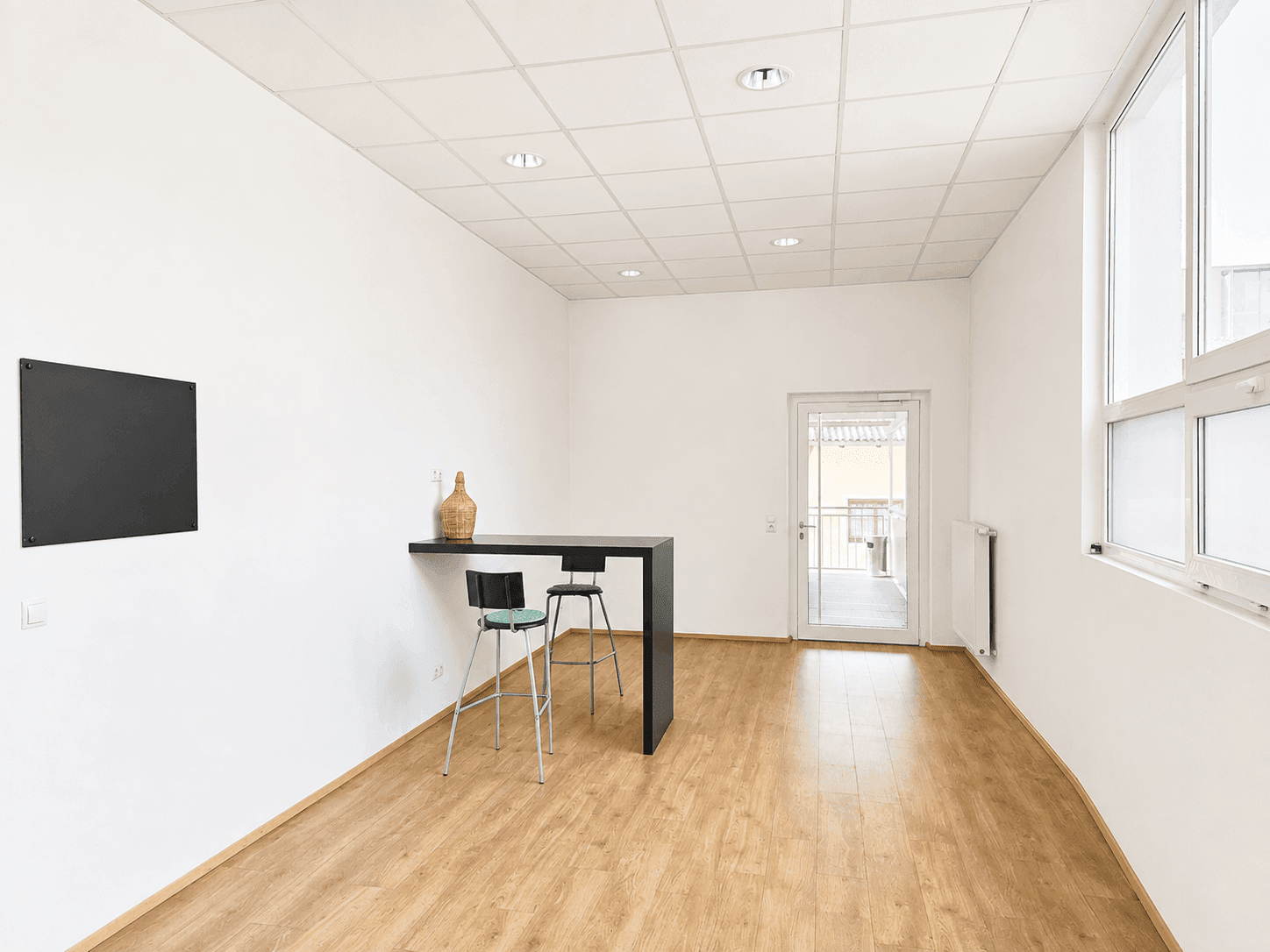 Kleinerer Bereich eines Gewerberaums mit Bartisch, Hockern und Zugang zu einem Balkon.