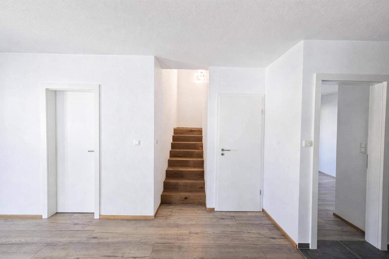 Heller Flurbereich mit Holztreppe und mehreren Türen, der verschiedene Räume miteinander verbindet.