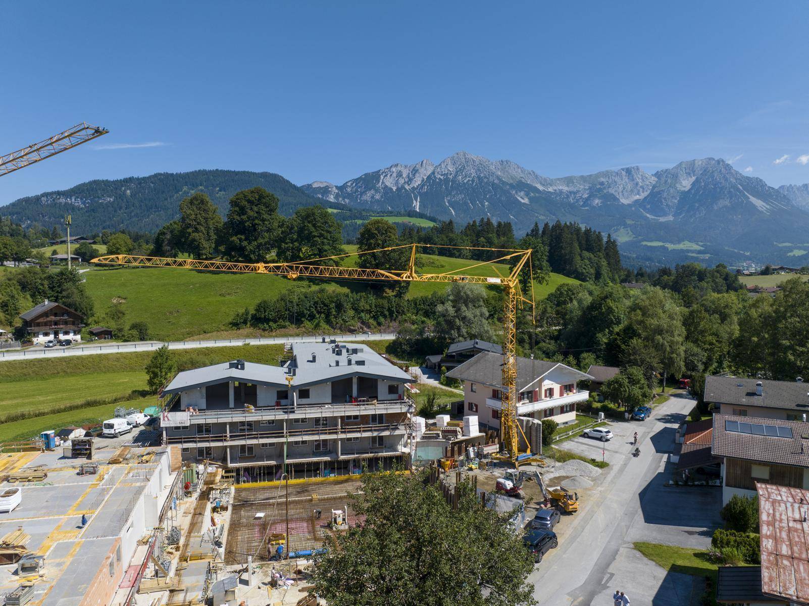 Luftaufnahme einer Baustelle mit Kränen vor der Kulisse einer beeindruckenden Berglandschaft.