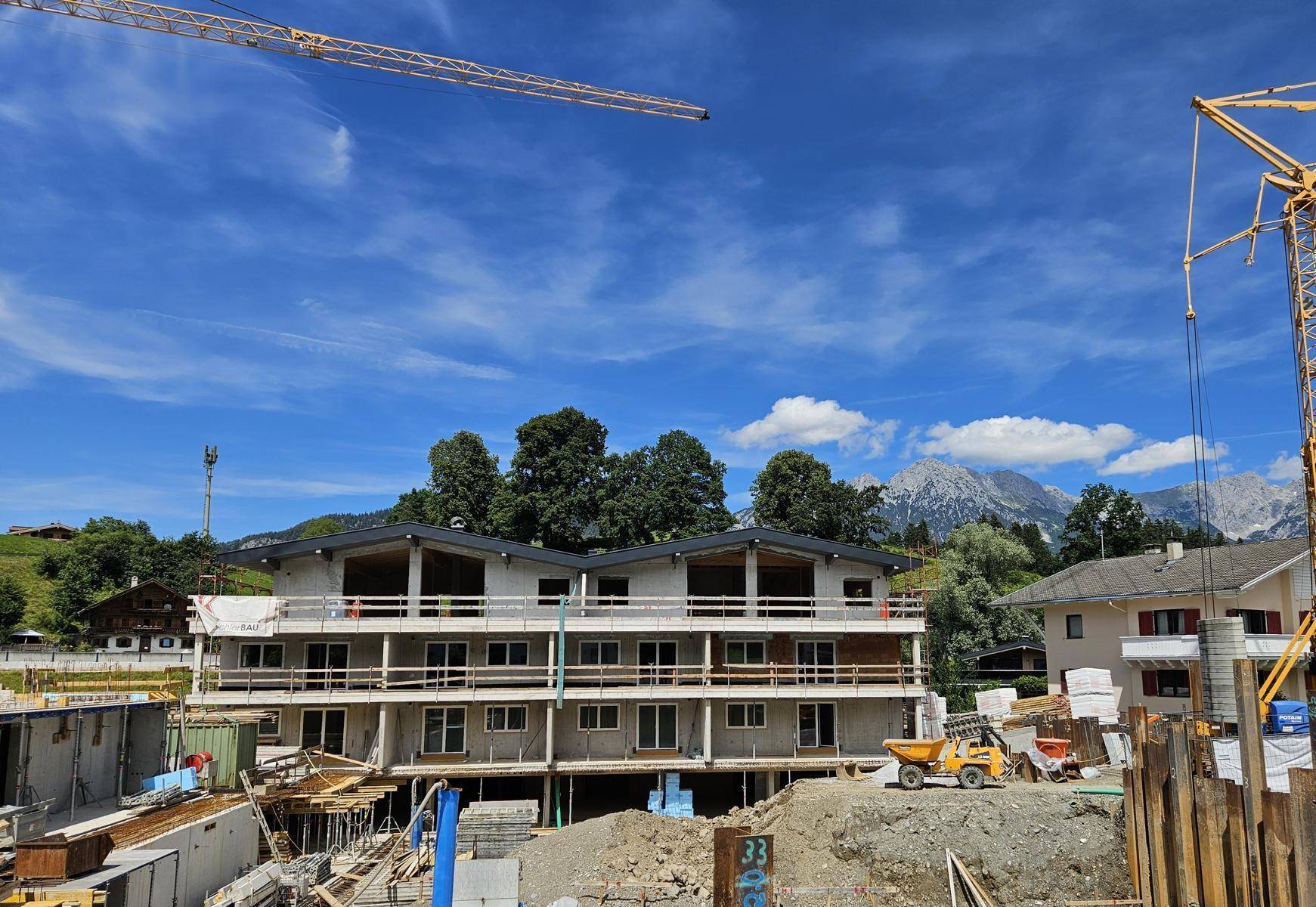 Baustelle eines neuen Gebäudes mit Blick auf die majestätischen Berge unter einem klaren blauen Himmel.