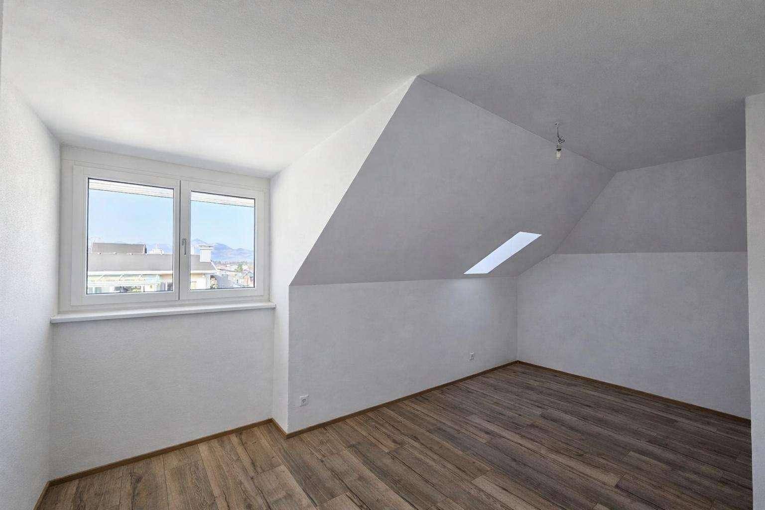 Leeres Schlafzimmer mit Dachschräge, Dachfenster und Holzfußboden.