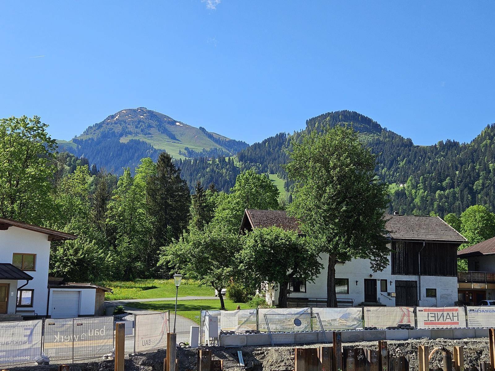 Blick auf die umliegende Berglandschaft mit grünen Hügeln und einem Bauprojekt im Vordergrund.